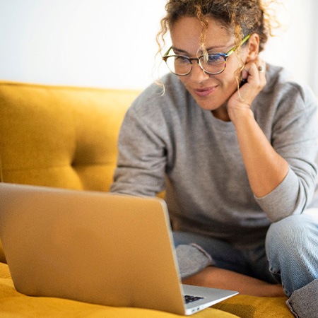 Woman smiling while working on laptop on couch