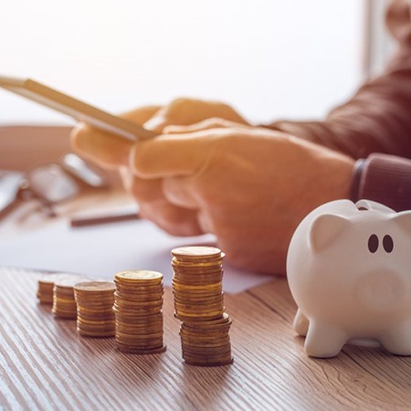 Man using his phone as a calculator with a piggy bank and coins on his desk