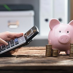 Close up of individual using a calculator with coin stacks and piggy bank on their desk