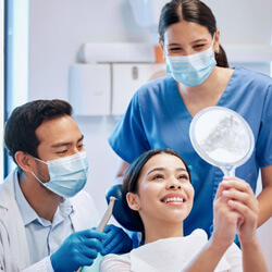 patient looking at reflection with dentist and dental assistant