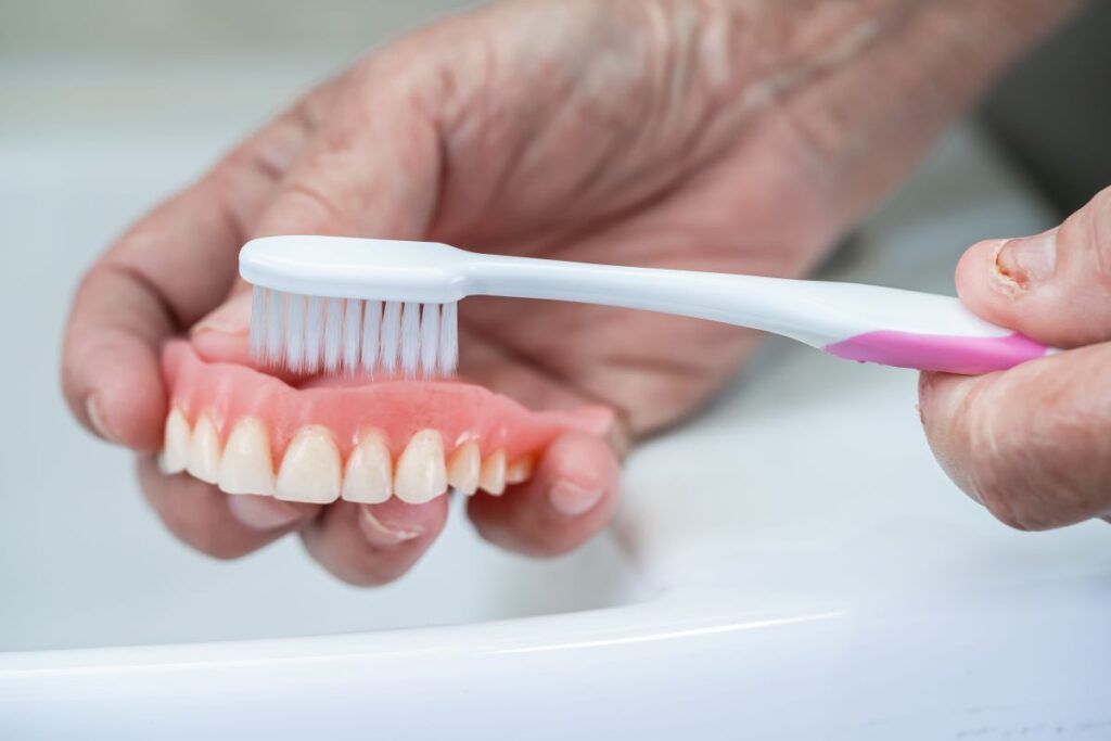 Hands brushing a pair of dentures with a toothbrush