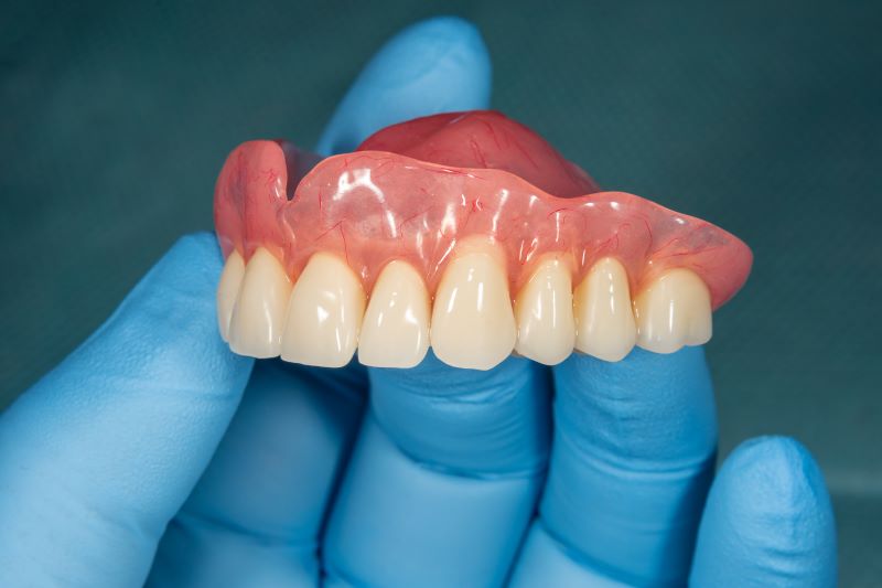 A hand with blue rubber gloves holding a denture.